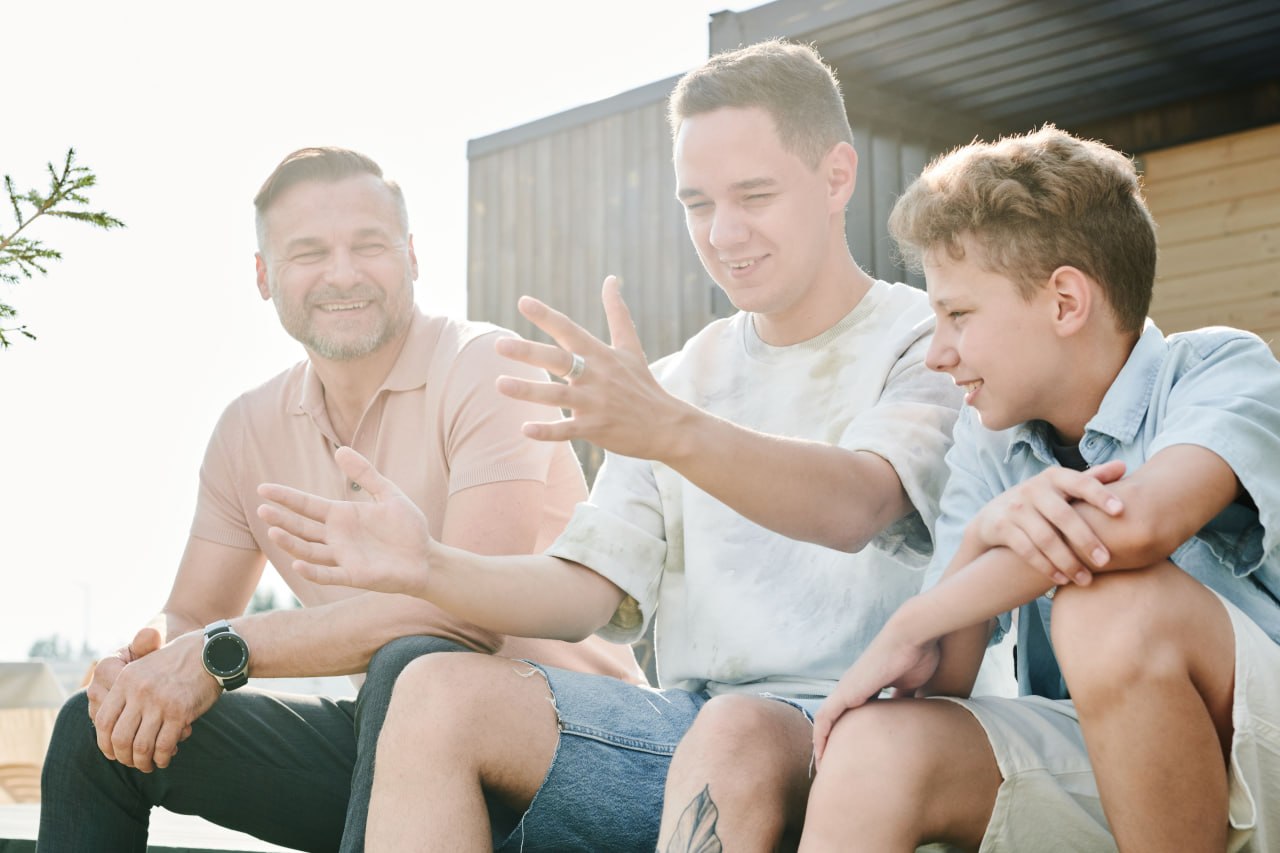An older man, a young adult, and a teen sitting outside talking